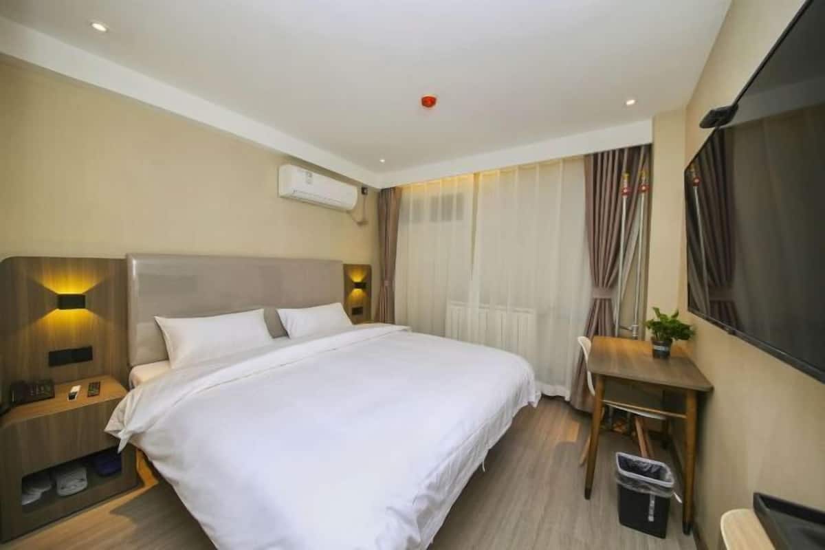 A hotel room with a large bed, bedside tables, a desk, and a TV.