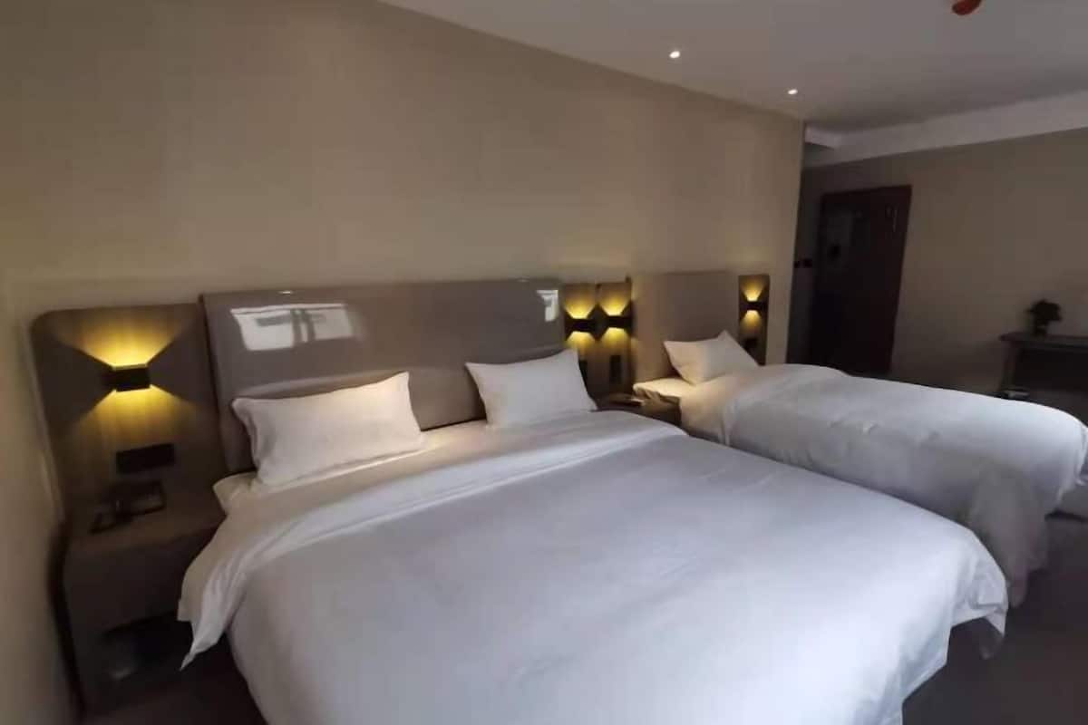 A hotel room with two beds, nightstands, and wall-mounted lighting.