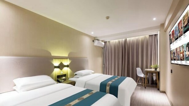 Een hotelkamer met twee bedden, een bureau, een stoel en een aan de muur bevestigde televisie.