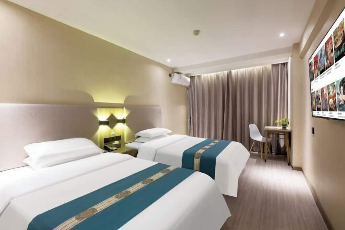 A hotel room with two beds, a desk, a chair, and a wall-mounted TV.