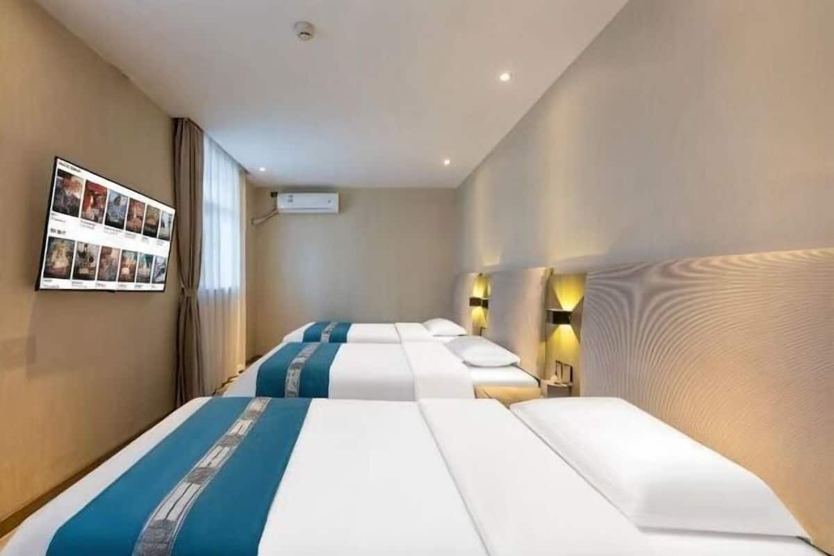 A hotel room with three beds, a wall-mounted TV, and a flat-screen TV on the wall.