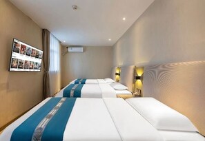 Une chambre d’hôtel avec trois lits, un téléviseur fixé au mur et un téléviseur à écran plat également fixé au mur.