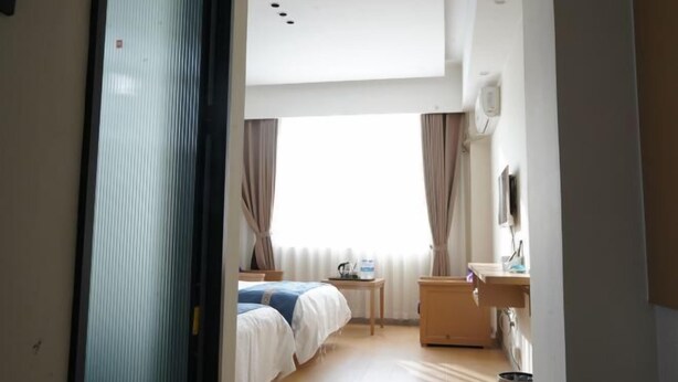 Hotelkamer met een bed, nachtkastje, een klein tafeltje met een lamp, een televisie en een raam met gordijnen.