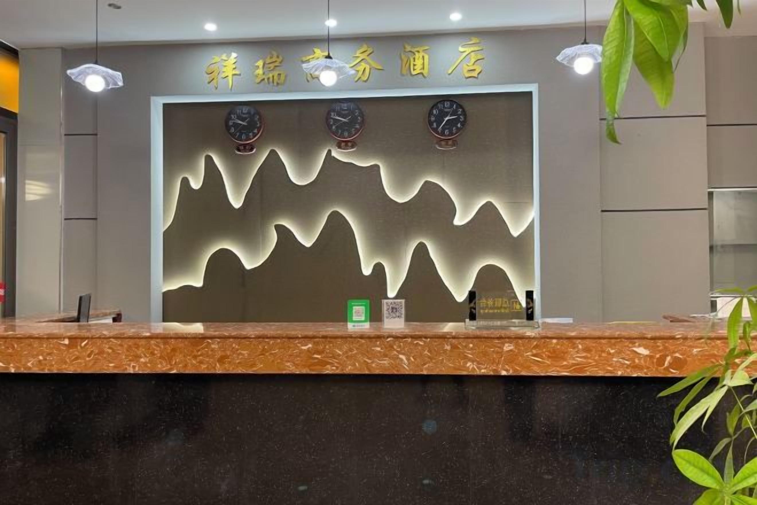 Un mostrador de recepción de hotel con un diseño moderno, que presenta un patrón de luz ondulado en la pared y tres relojes encima.