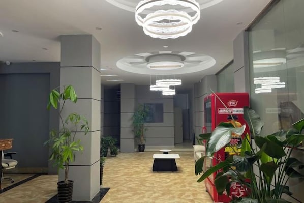 A lobby with a reception desk, potted plants, and a red vending machine.