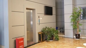 Een moderne lift met een digitaal display, een flatscreen televisie aan de muur en potplanten in een hal.