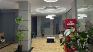 Een moderne lobby met een marmeren vloer, potplanten, een rode automaat en een wit receptiebalie.