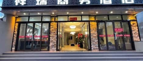 A hotel entrance with a sign in a foreign language, glass doors, and a staircase leading up to the entrance.