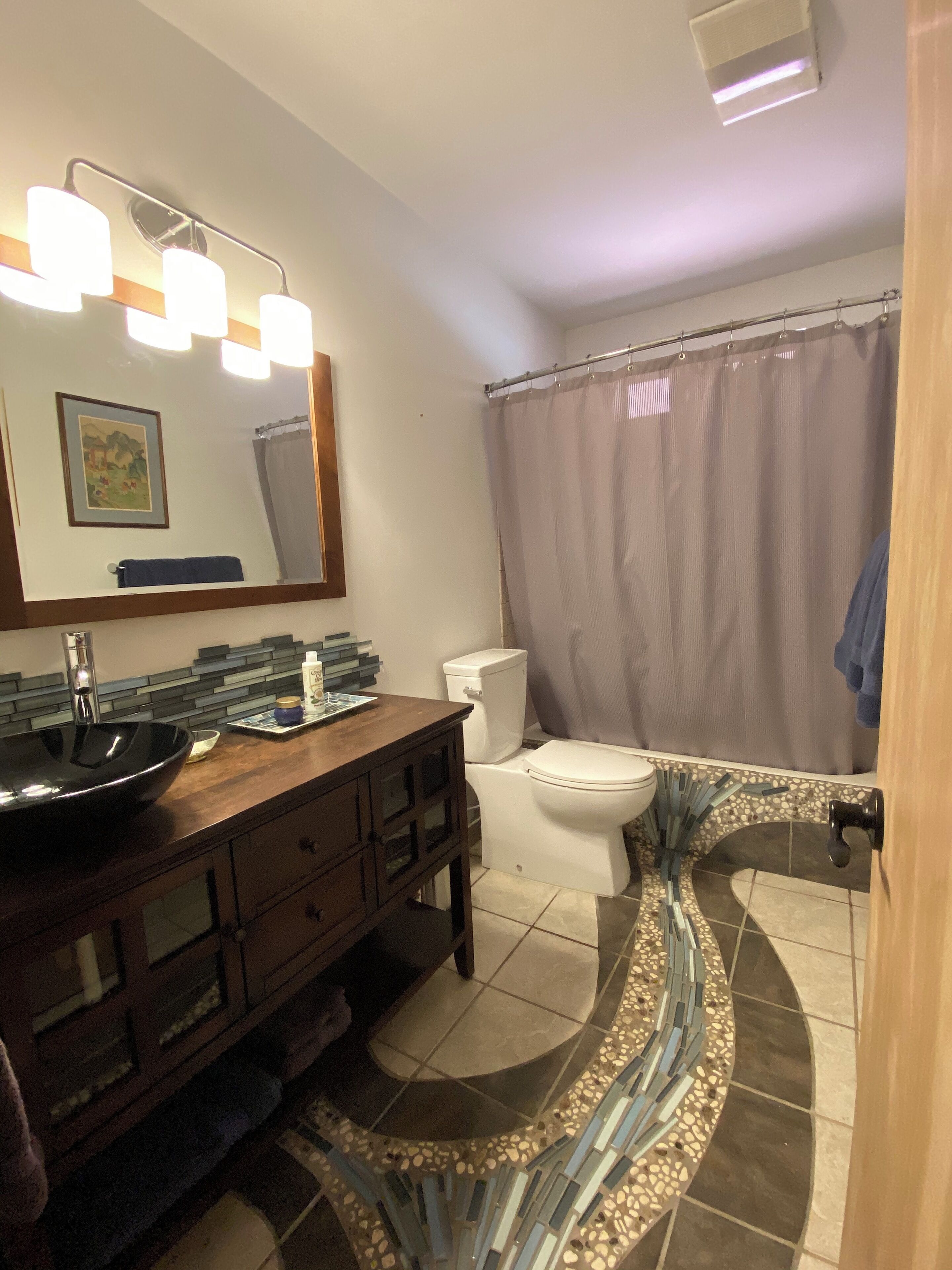 A bathroom with a vanity, sink, mirror, toilet, and shower curtain.