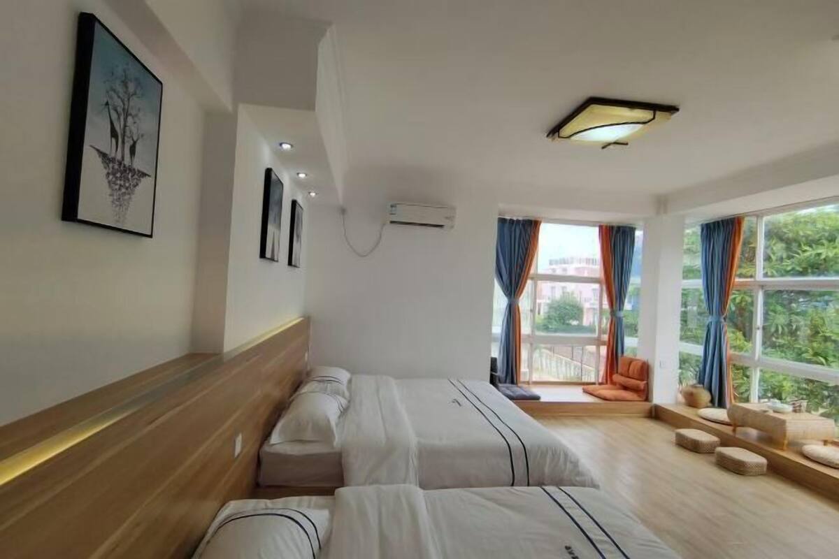 Ein Hotelzimmer mit zwei Betten, einer hölzernen Bank, einem Fenster mit Vorhängen und einer Deckenleuchte.