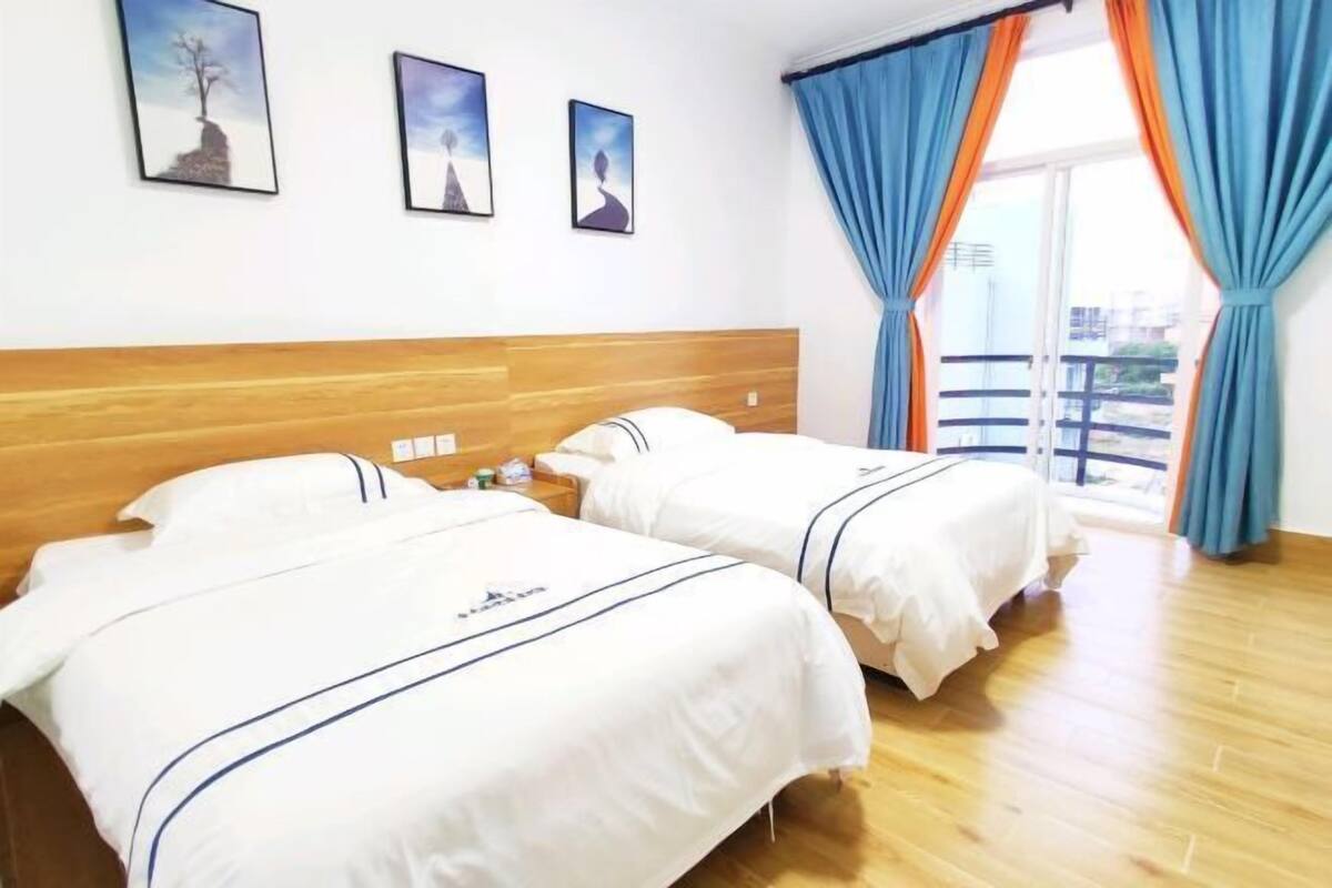 Ein Hotelzimmer mit zwei Betten, einem hölzernen Kopfteil und einem Balkon mit blauen Vorhängen.
