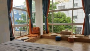 Un dormitorio con una cama grande, un asiento junto a la ventana con cojines y vistas a edificios y árboles.