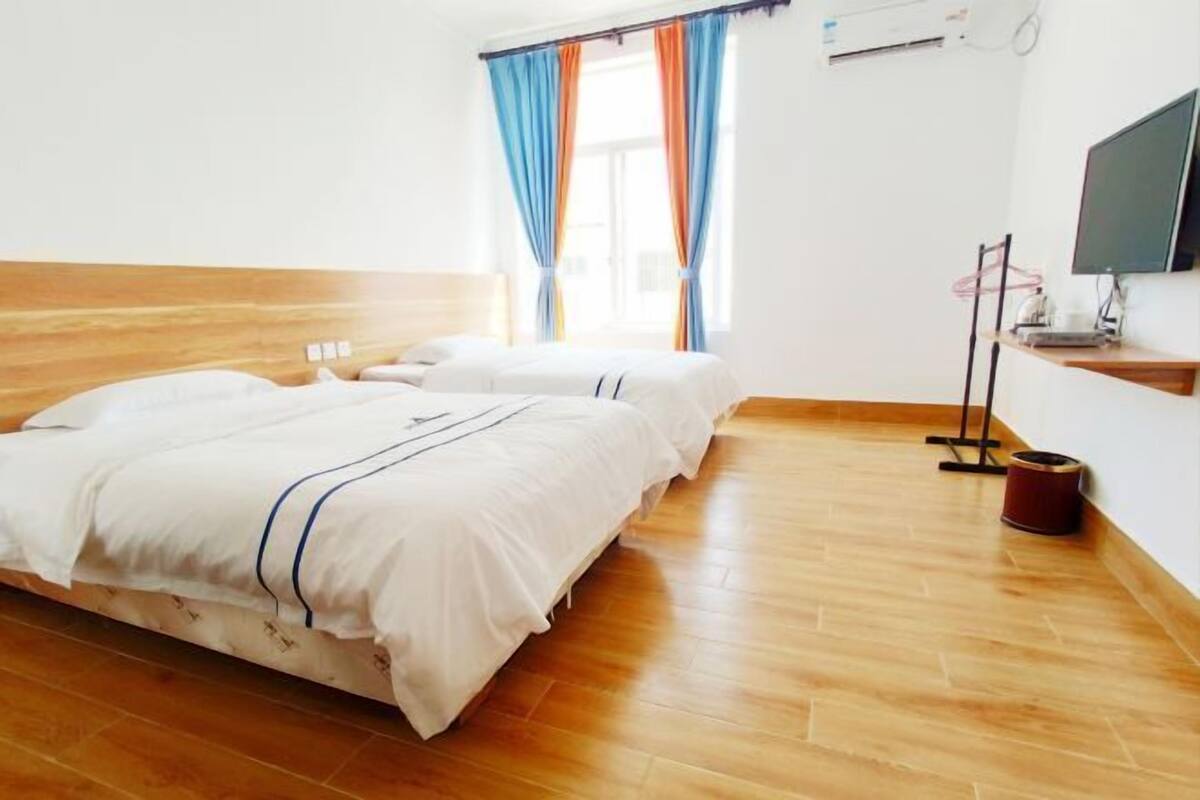 Ein Hotelzimmer mit zwei Betten, Holzboden, einem Fernseher und einem Fenster mit Vorhängen.