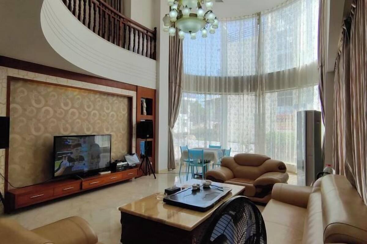 Ein geräumiges Wohnzimmer mit großem Fernseher, bequemen Sitzgelegenheiten und einem Balkon mit Vorhängen.