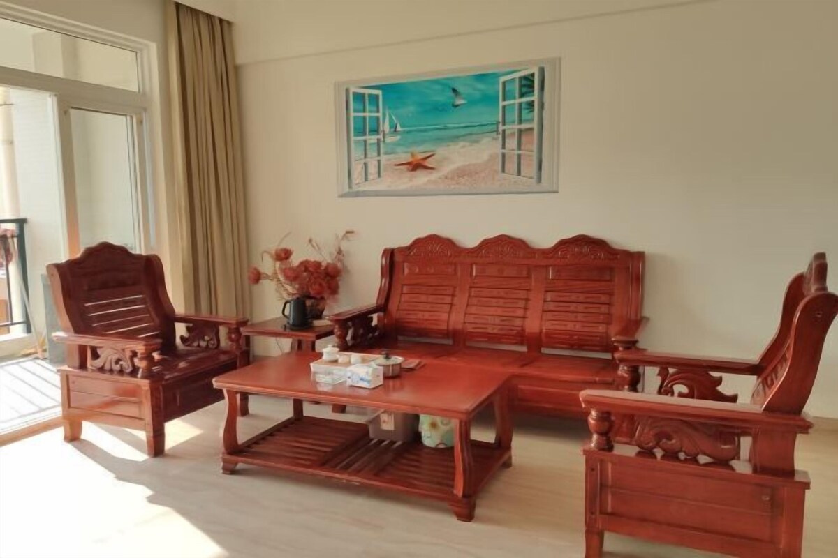 A room with a wooden sofa set, a coffee table, and a painting of a beach scene.