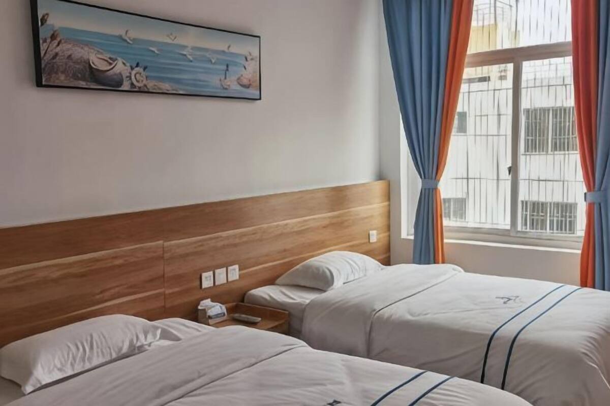 Ein Hotelzimmer mit zwei Betten, einem Holzkopfende, einem Gemälde an der Wand und einem Fenster mit Vorhängen.