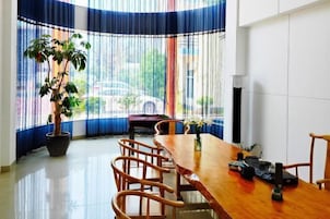 Uma área de refeições com mesa de madeira, cadeiras, planta em vaso e janela com cortinas.