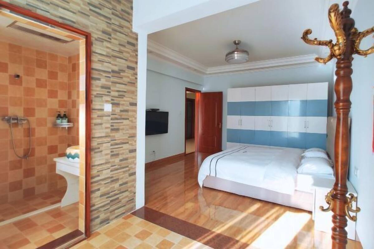 Ein Schlafzimmer mit einem Bett, einem Holzschrank, einem Badezimmer mit Dusche und einem Spiegel.