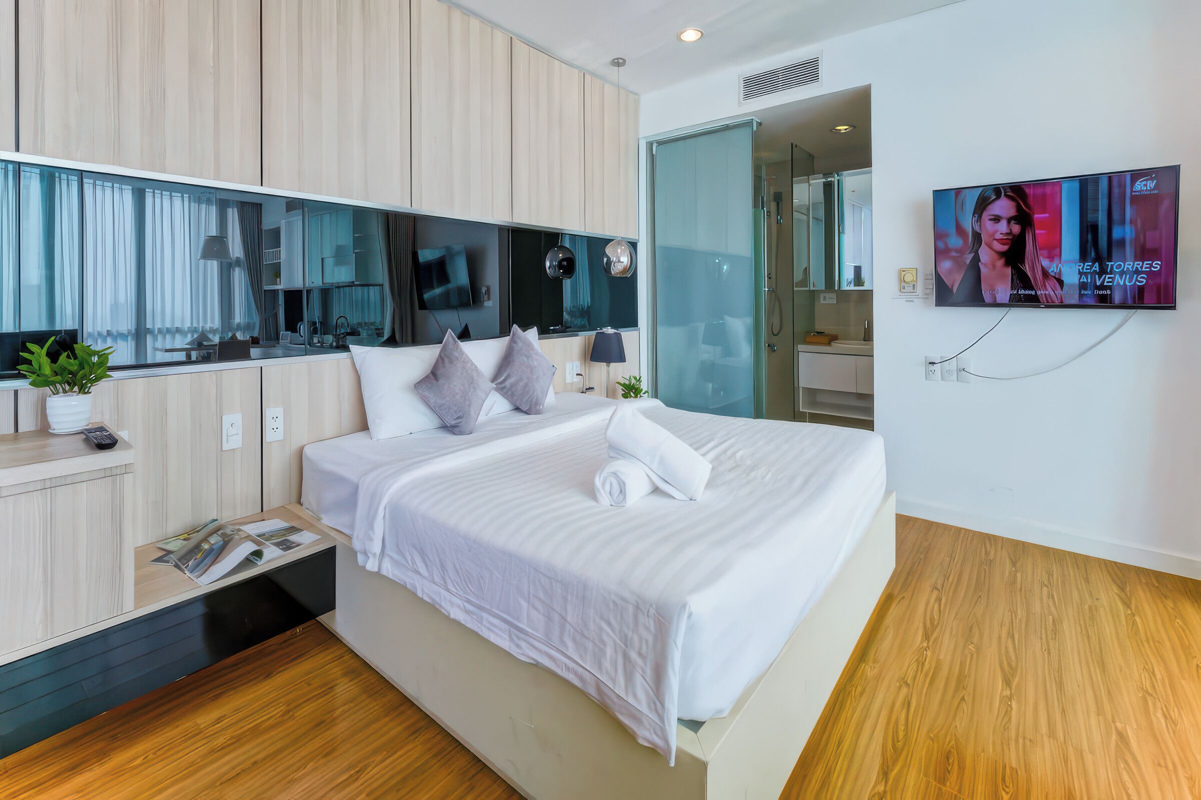 Une chambre d’hôtel moderne avec un grand lit, un téléviseur fixé au mur et un plancher en bois.