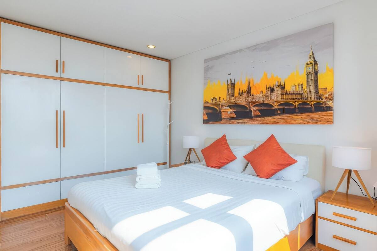 A hotel room with a large bed, white wardrobe, and a painting of a bridge.