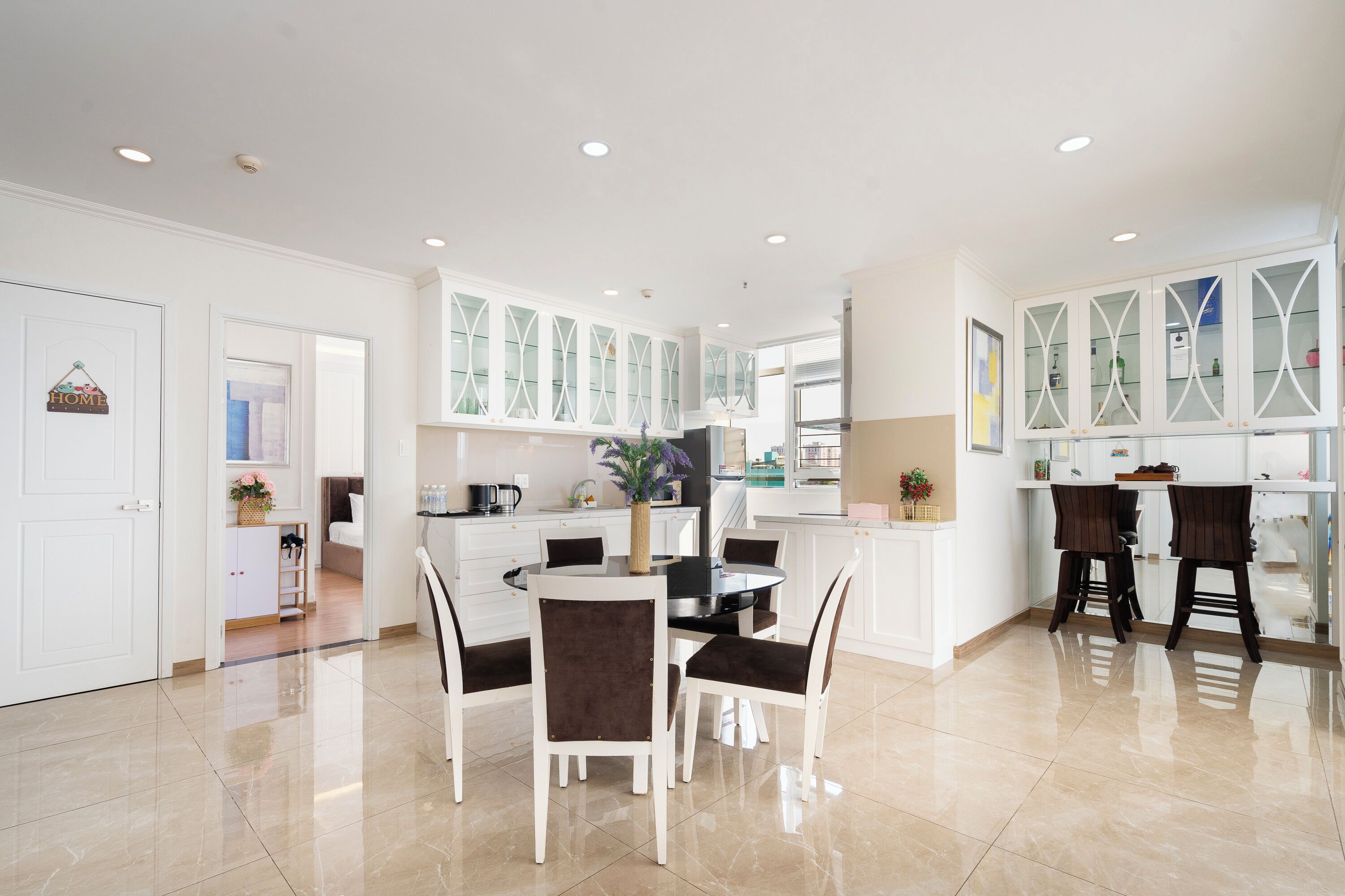 A modern kitchen with white cabinetry, a dining area with a round table and chairs, and a kitchen island with stools.