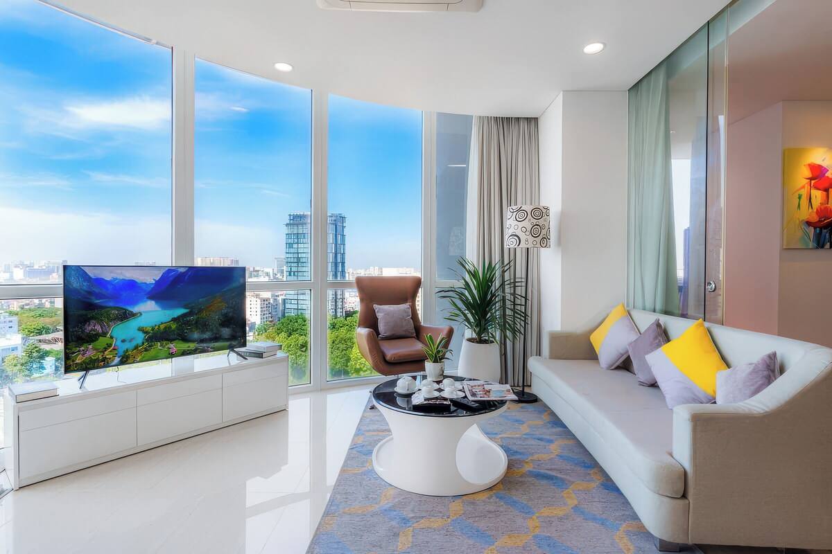 A modern living room with a large TV, a sofa, a coffee table, and a view of the city through large windows.