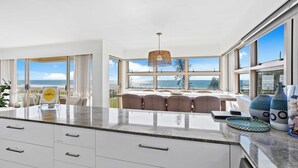 A modern kitchen with a large island, a dining area with a view of the ocean, and a hanging light fixture. - Surfsong on Miami Beach (Miami)