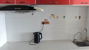 Een keuken met rode kastjes, een zwarte waterkoker, een spoelbak en een wandcontactdoos.