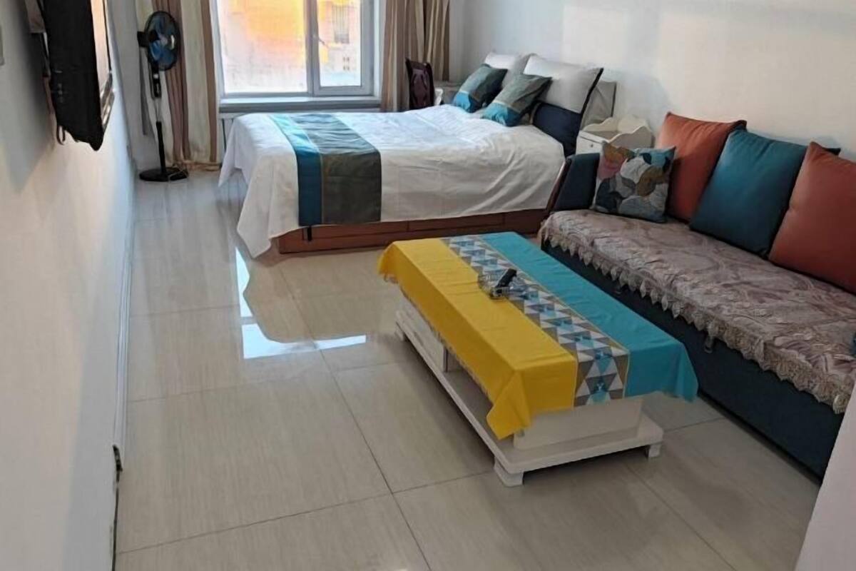 Een hotelkamer met een bed, een bank, een klein tafeltje en een ventilator.