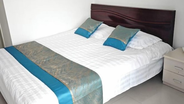 Een net opgemaakt bed met een donker hoofdbord, wit beddengoed en twee decoratieve kussens.