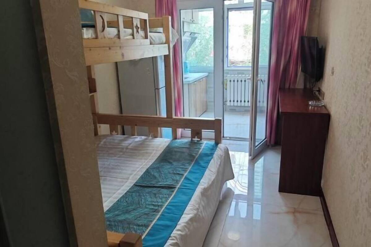 Een kamer met een stapelbed, een klein bureau, een televisie en een schuifdeur naar een buitenruimte.