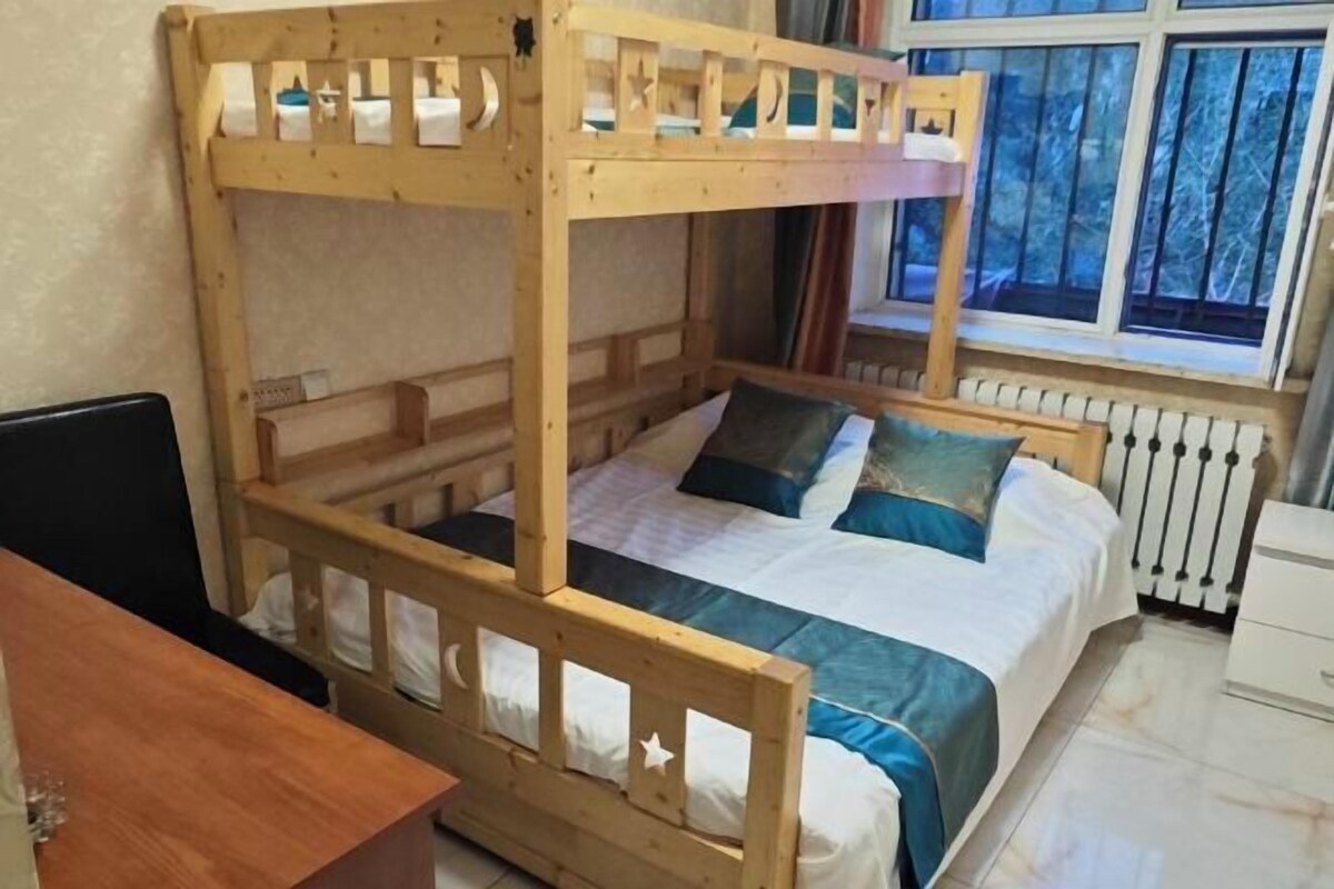 Een stapelbed met houten frame, een bureau en een raam met uitzicht op bomen.