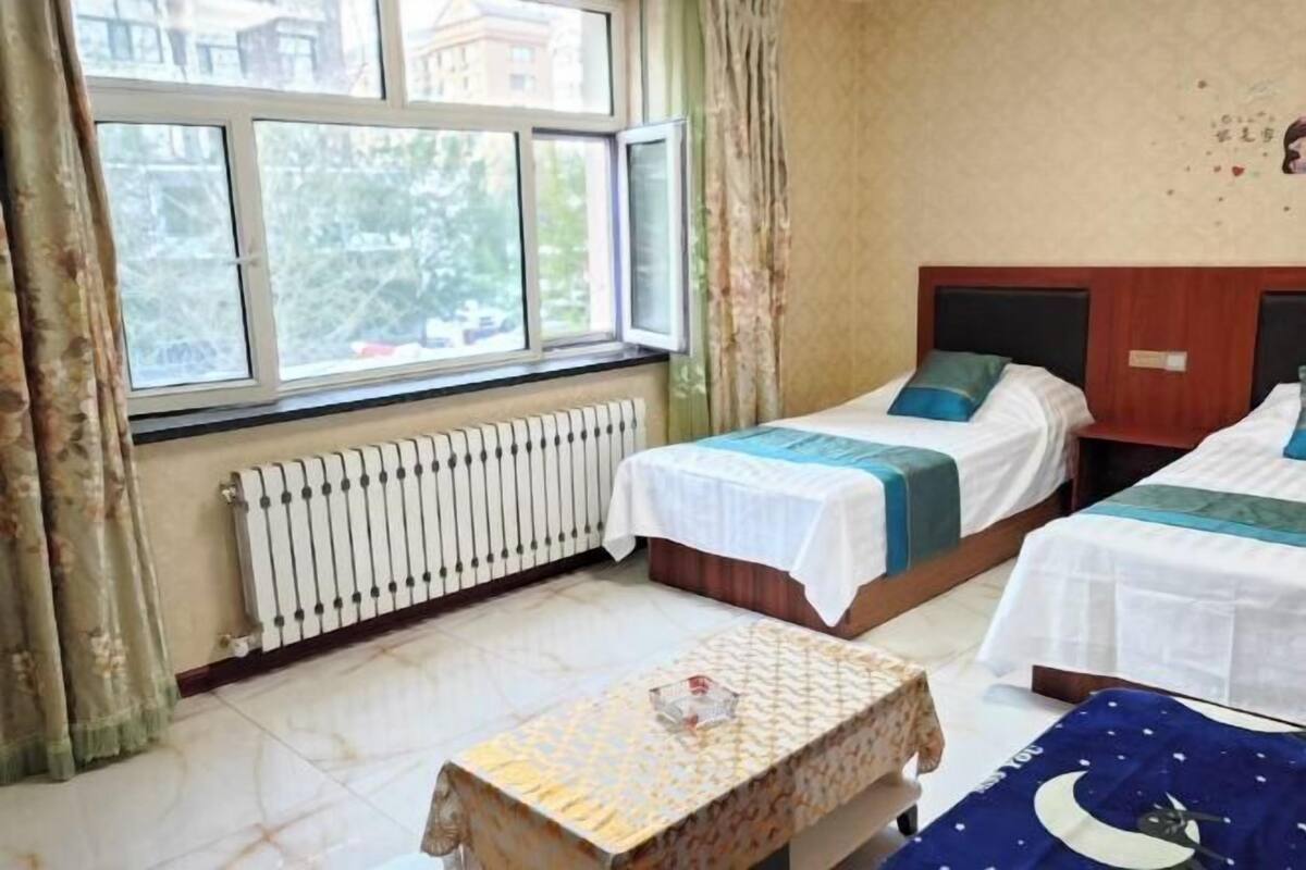 Een kamer met twee bedden, een radiator, een raam met gordijnen en een kleine tafel.