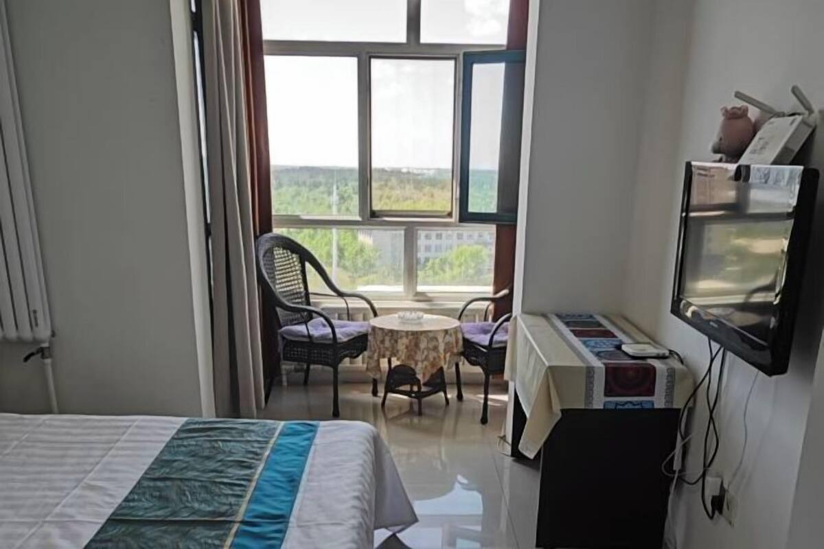 Een hotelkamer met een bed, een tafeltje, twee stoelen, een televisie en een balkon met uitzicht.