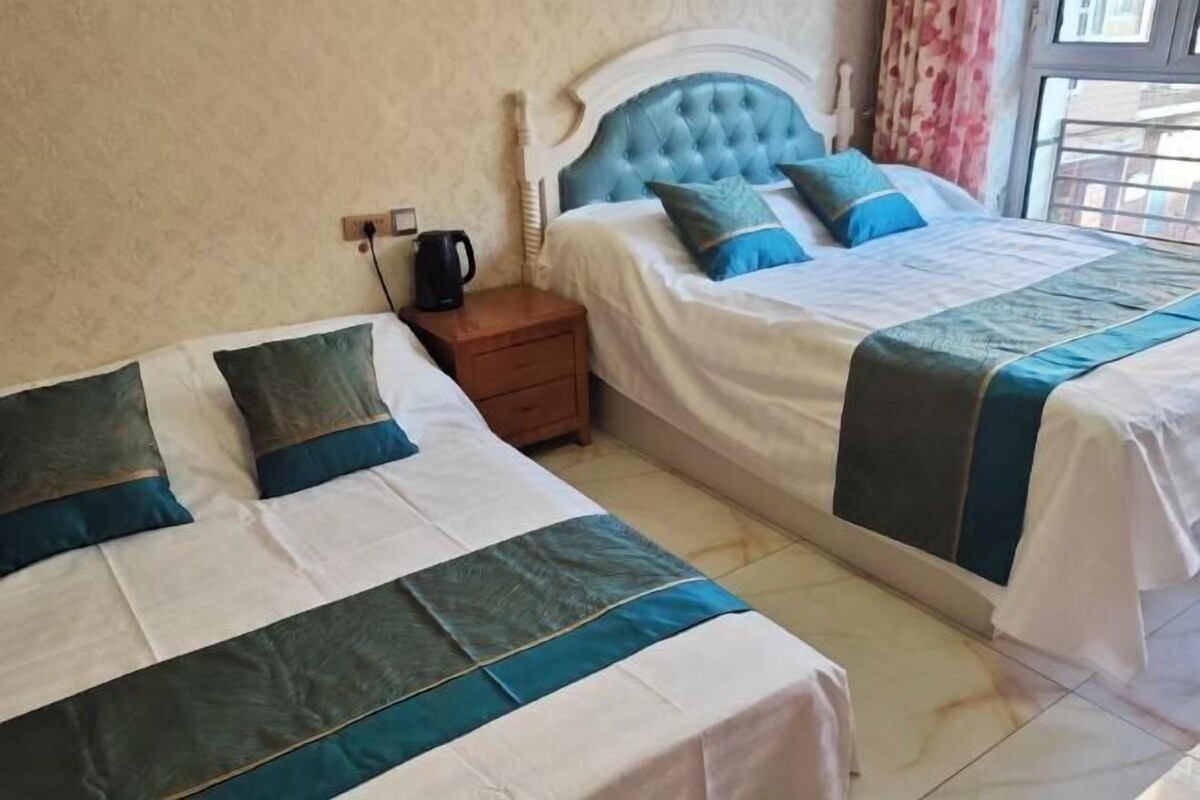 Een hotelkamer met twee bedden, een nachtkastje, een waterkoker en een raam met gordijnen.