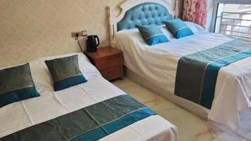 Habitación de hotel con dos camas, una mesita de noche, una tetera y una ventana con cortinas.