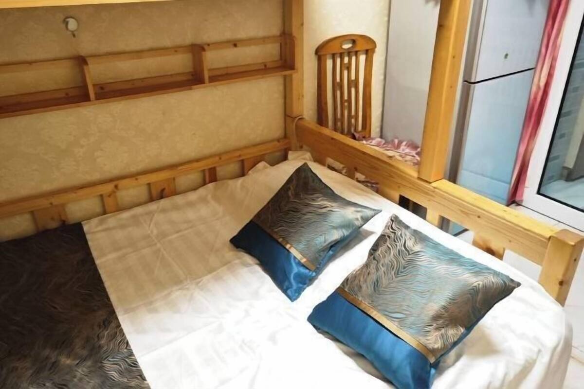Een bed met een houten hoofdbord, twee decoratieve kussens en een witte lakenset.