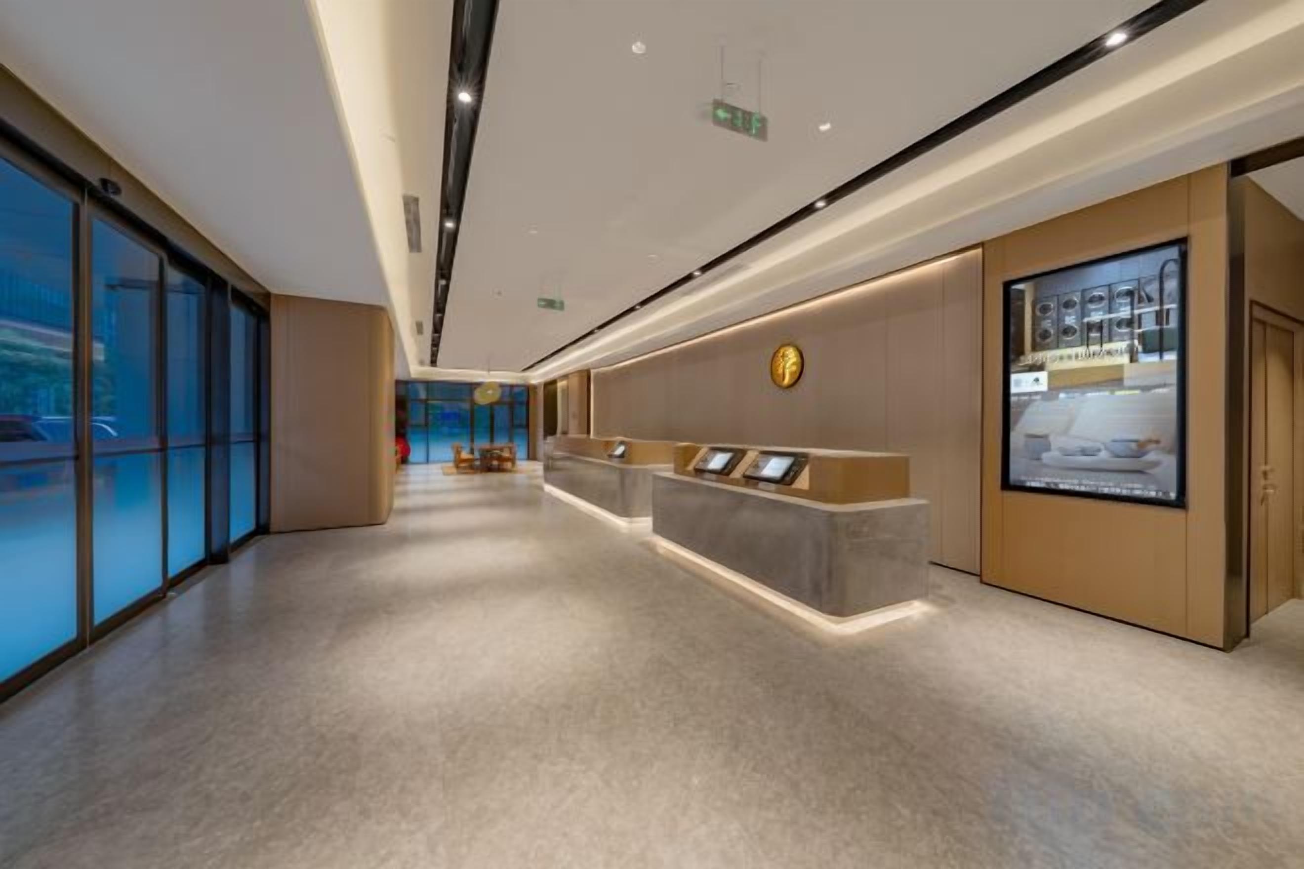A hotel reception area with a reception desk, a digital display, and a large window offering a view of the street.