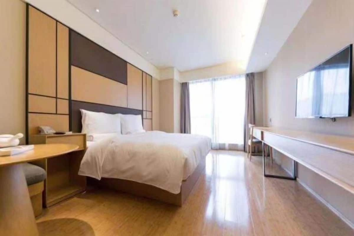 Ein modernes Hotelzimmer mit Bett, Nachttisch, Fernseher und einem großen Fenster.