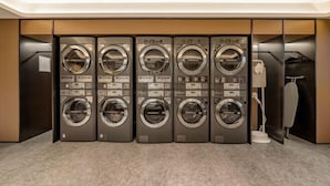 A row of five front-loading washing machines in a modern, well-lit laundry room with a marble floor. - JI Hotel (Chengdu Global Center) (Chengdu)