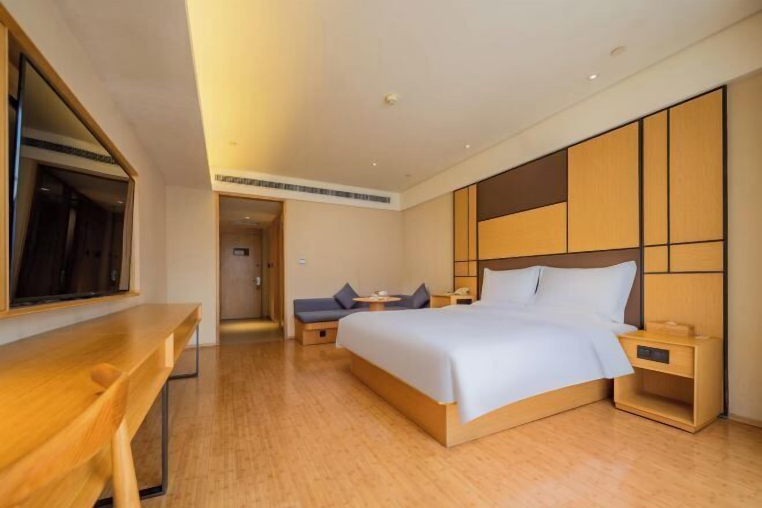 A modern hotel room with a wooden bed, bedside tables, a desk, and a large mirror.