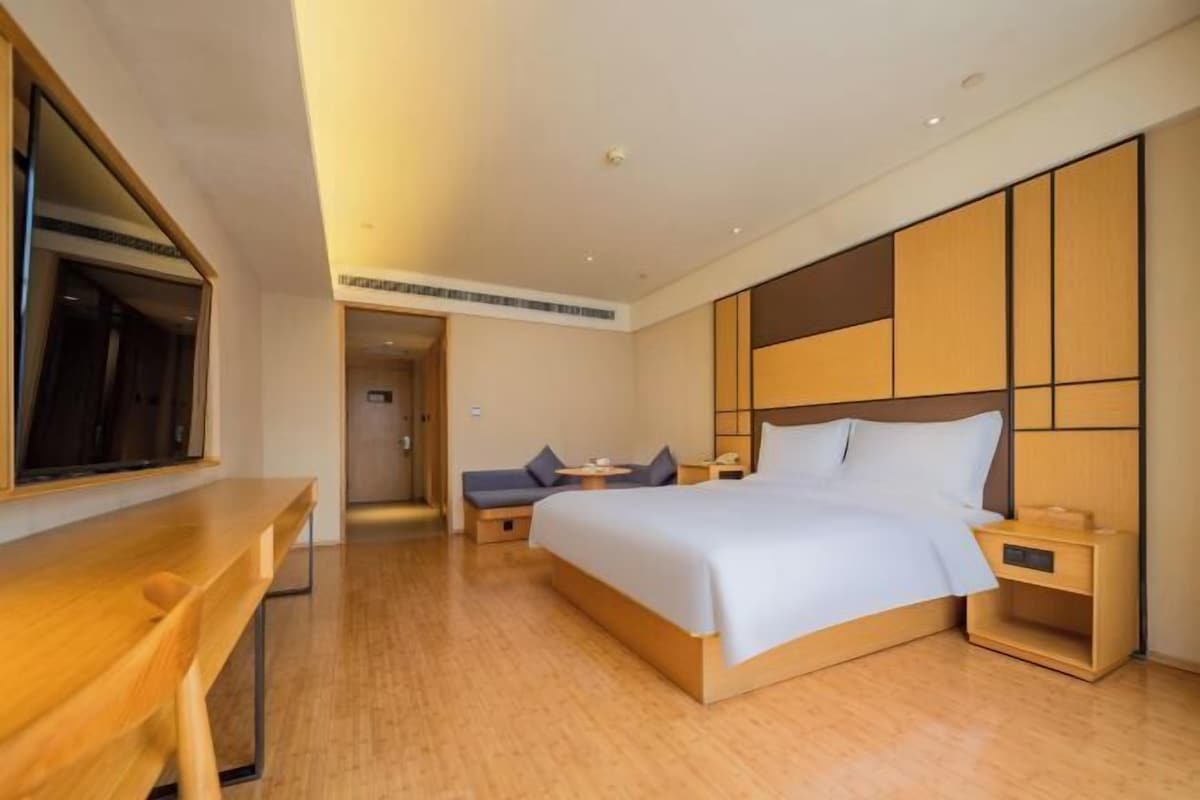 A modern hotel room with a wooden bed, bedside tables, a desk, and a large mirror.