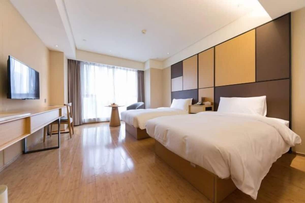 Ein Hotelzimmer mit einem großen Bett, einem Schreibtisch, einem Stuhl, einem Fernseher und einem Fenster mit Vorhängen.