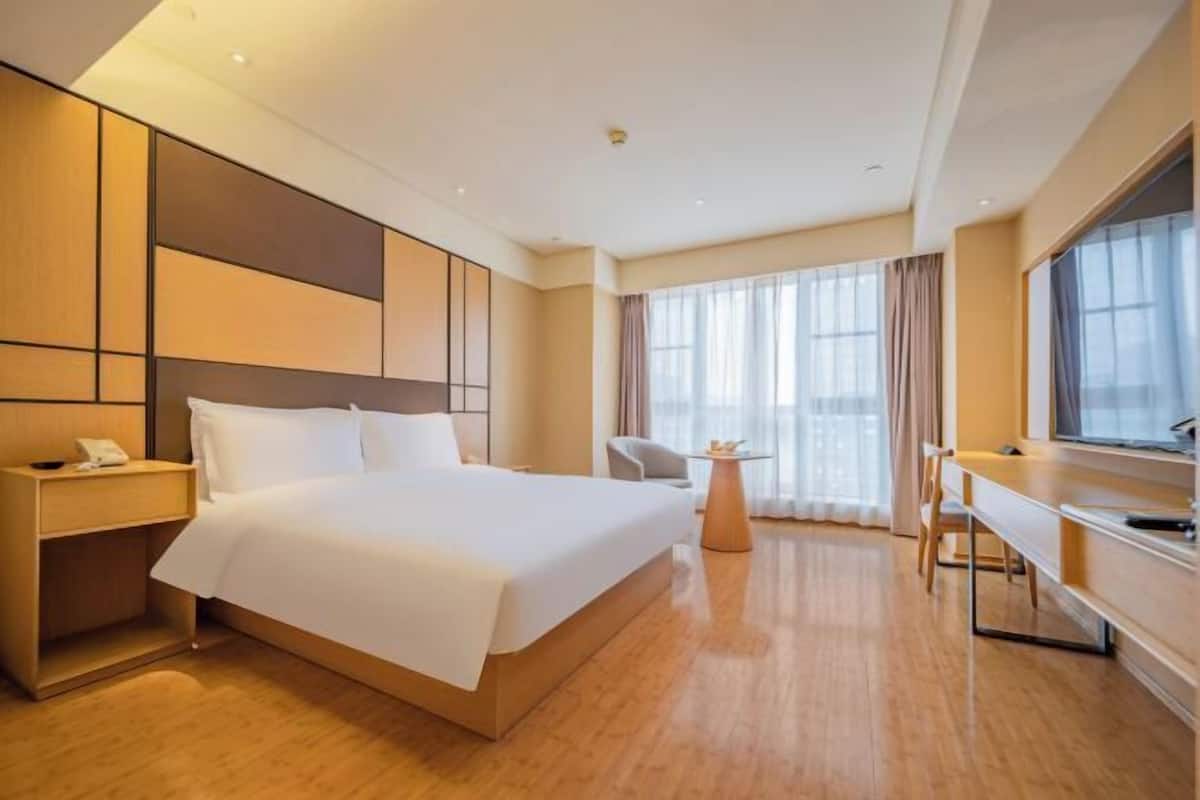 Ein Hotelzimmer mit Bett, Nachttisch, Schreibtisch, Stuhl und großen Fenstern.