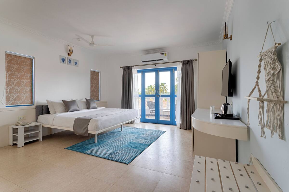 A bedroom with a bed, a desk, a chair, a TV, and a window with curtains.