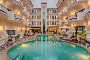 A large indoor swimming pool with a central fountain, surrounded by multiple balconies with outdoor seating and potted plants. - Azalea By Stone Wood Carmona (Varca)