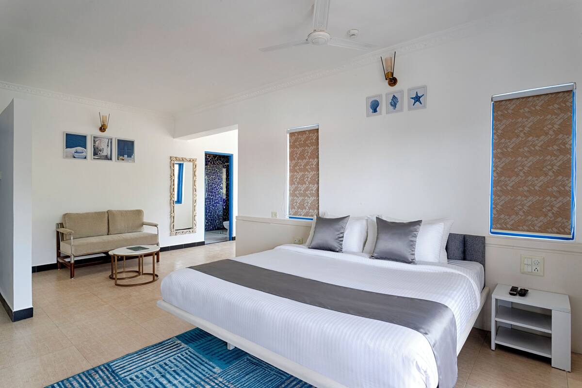 A modern hotel room with a large bed, a sofa, a small table, and a nightstand.