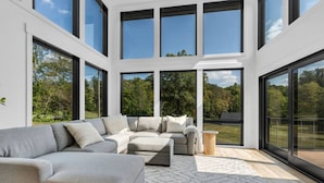 A modern living room with a sectional sofa, large windows, and a view of greenery. - Luxury Escape, Hot Tub, Fireplace, Espresso Bar (Ickesburg)