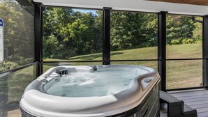 A hot tub in a covered outdoor area with a view of a grassy field and trees. - Luxury Escape, Hot Tub, Fireplace, Espresso Bar (Ickesburg)