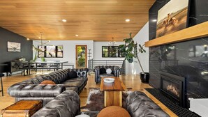 Una sala de estar moderna con techo de madera, sofás de cuero, chimenea y comedor con vistas a zonas verdes.